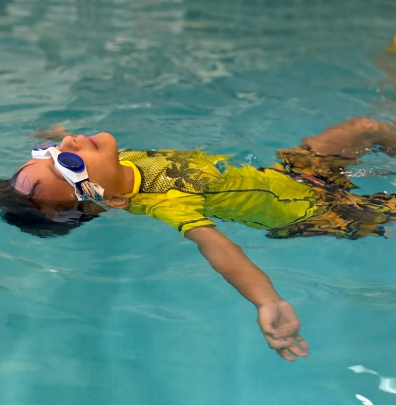 Preschool swimmer in goggles floating on her back