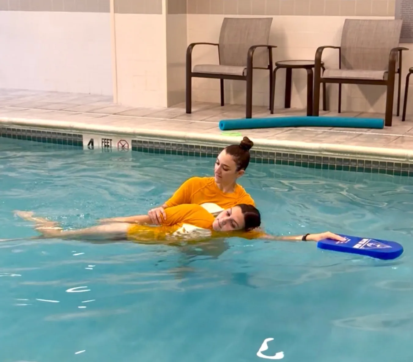School-age swimmer kicking with a kickboard beside an instructor