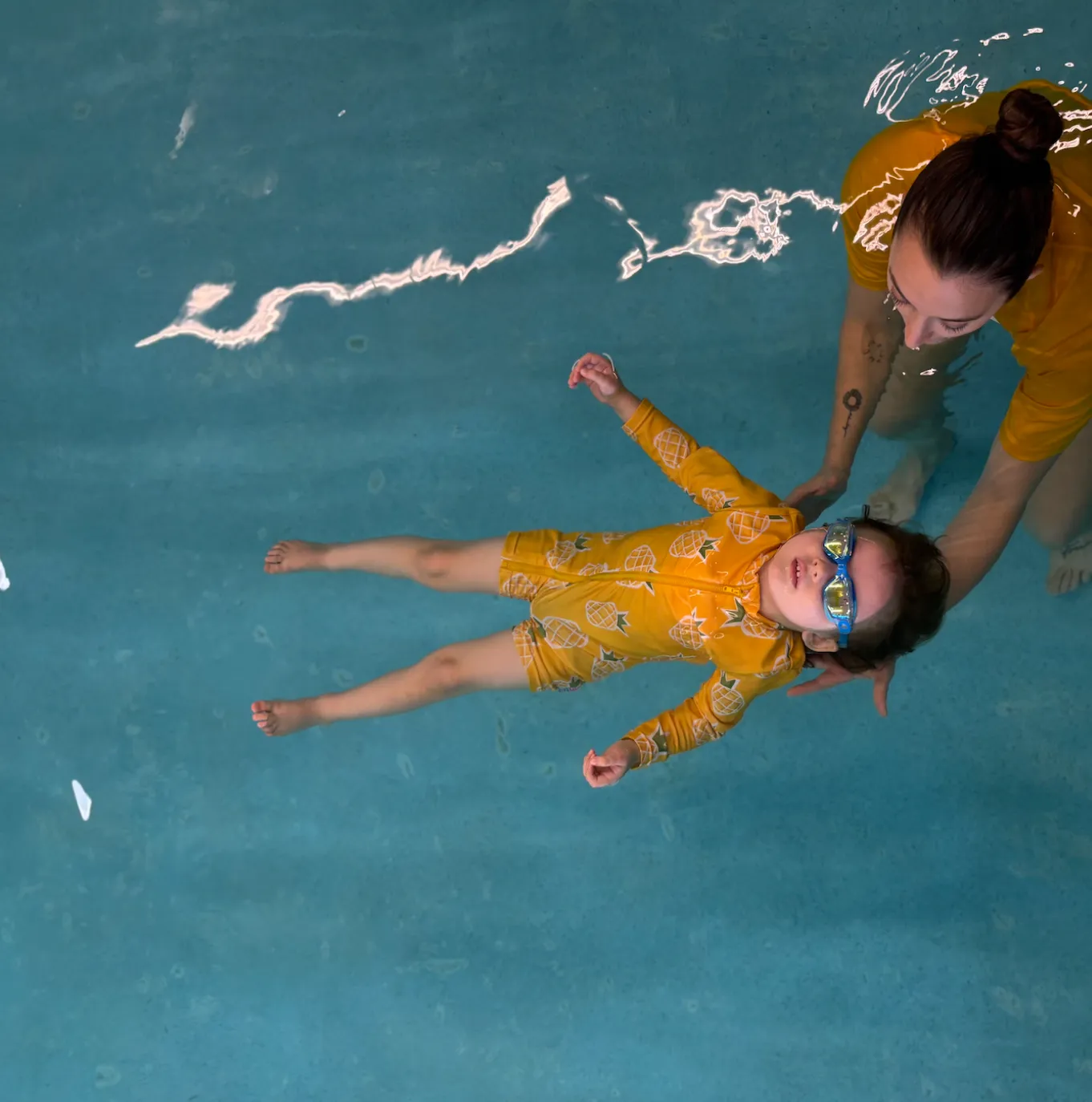 Toddler in goggles floating on her back with an instructor